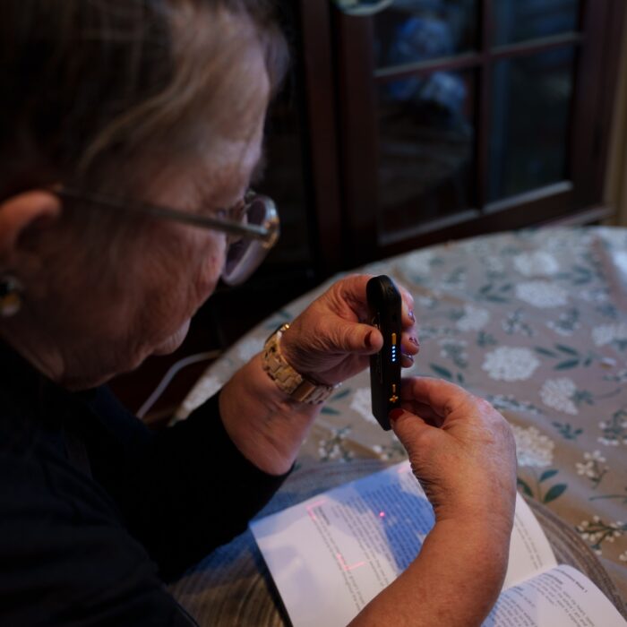 Woman holding a small reader device while looking at an open book on a table